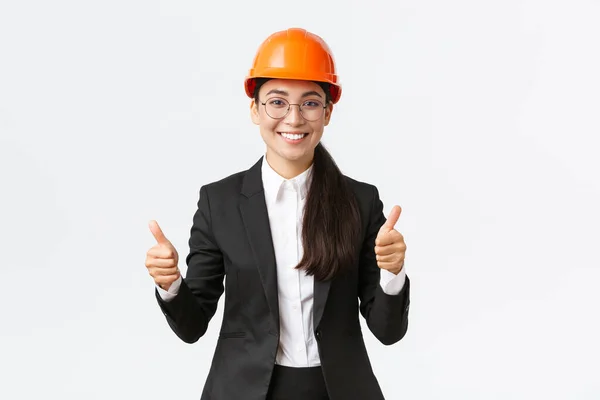 Uitstekend werk, goed werk. Tevreden professionele vrouwelijke ingenieur, bouwkundige in veiligheidshelm en pak, met duim omhoog in goedkeuring, adverteren huis te koop, witte achtergrond — Stockfoto