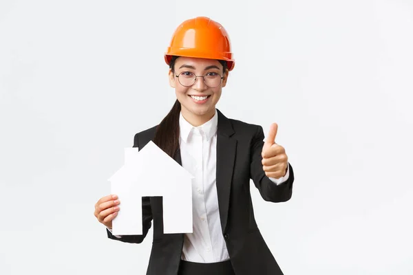 Porträt einer jungen asiatischen Bauingenieurin, Architektin mit Schutzhelm und Businessanzug, die nach Hause geht und Daumen nach oben zeigt, um den Hausbau zu fördern — Stockfoto