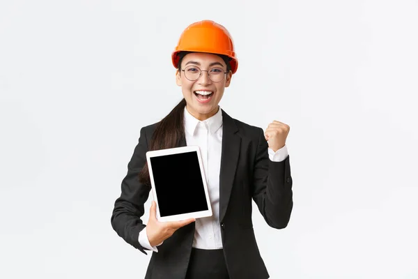 공장에서 성공적으로 일하는 여성 기술자, 안전모와 사업용 슈트 주먹 펌프의 건설 책임자, 업적에 대해 승리하는 모습, 디지털 태블릿 디스플레이, 그래프 또는 다이어그램 — 스톡 사진