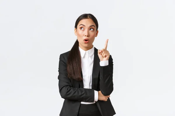 Smart and creative asian businesswoman have excellent idea, raising finger up and looking upper left corner thoughtful, suggest solution, make plan, saying thought over white background — Stock Photo, Image