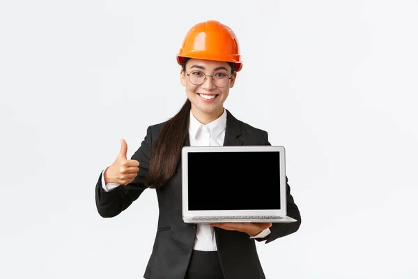 Smiling arquiteto profissional feminino, gerente de construção na fábrica mostrando gráfico, diagrama positivo, fazer polegar-se na aprovação e segurando tela de rosto laptop, usar capacete de segurança — Fotografia de Stock