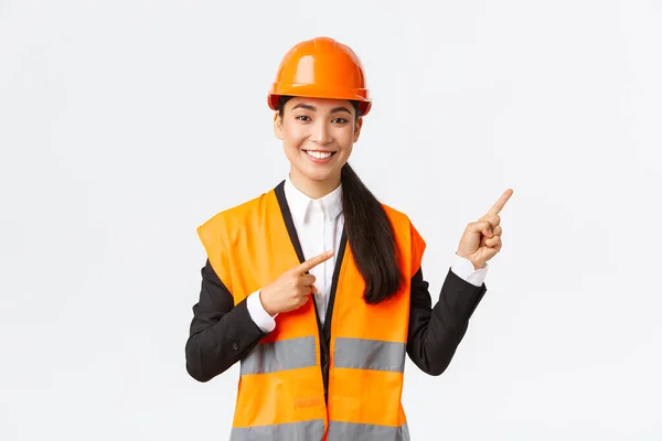 建築、建設、産業の概念。安全ヘルメットとオブジェクトを示す反射服で笑顔の女性アジアのエンジニアは、右の指を指して、セールスマンはクライアントに不動産を紹介 — ストック写真