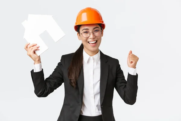 Erfolgreiche asiatische Bauingenieurin, Teamleiterin Architektin, die ihr Ziel erreicht, Häusermachet und Faustpumpe in der Hand, Sieg in Helm und Businessanzug feiernd — Stockfoto