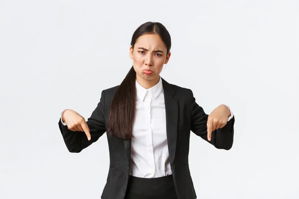 Disappointed sulking asian businesswoman complaining on unfair situation. Female entrepreneur in suit pointing fingers down and grimacing displeased, standing upset white background — Stock Photo, Image