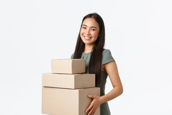 Kleinunternehmer, Start-up und Arbeit von zu Hause aus. Lächelnde junge Filialleiterin, asiatische Geschäftsfrau sammelt Pakete, verpackt Bestellungen in Kartons und trägt sie zum Zusteller — Stockfoto