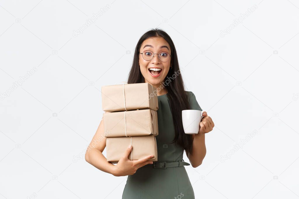 Excited smiling asian female drinking coffee and carry piles of boxes for shipping to clients, small business owner manage customer purchases and packing it, give items to courier, white background