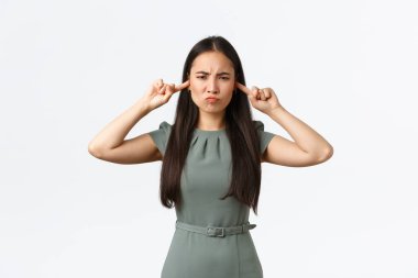 Küçük işletme sahipleri, kadın girişimciler konsepti. Sinirli ve rahatsız Asyalı bir kadın, komşularının tadilat gürültüsünden şikayetçi, buruşuk, hoşnutsuz ve parmaklarıyla kulaklarını tıkamış.