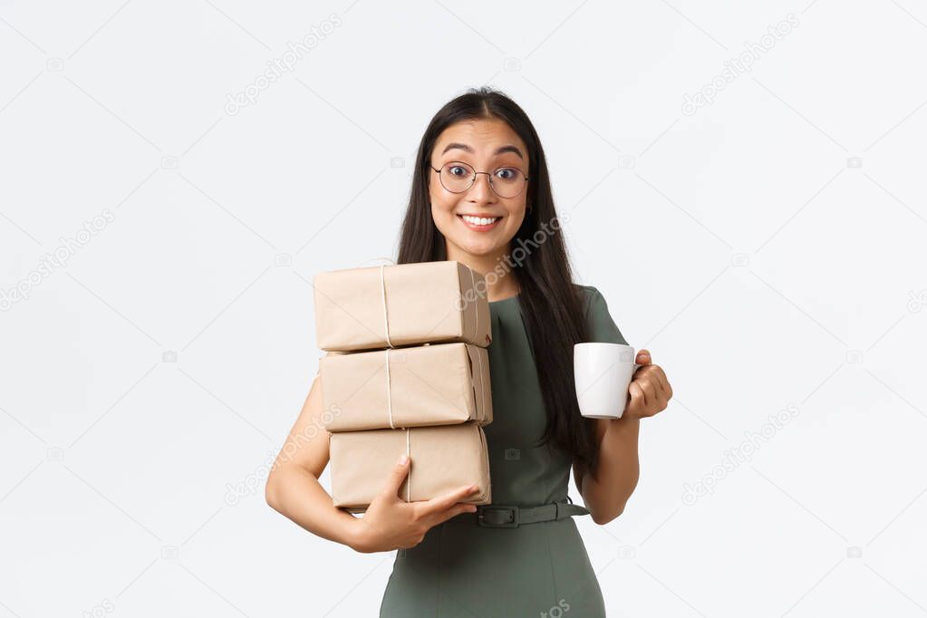 Smiling funny asian businesswoman, small business owner drinking coffee and carry boxes for shipping, pack delivery for customers, manage shopping site, standing white background