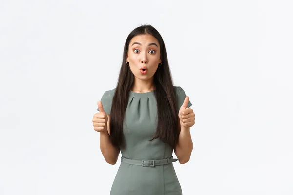 Proprietários de pequenas empresas, conceito de mulheres empresárias. Surpreendido e impressionado asiático fêmea no vestido mostrando polegares para cima e olhando espantado com grande trabalho, de pé fundo branco — Fotografia de Stock