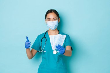 Covid-19, sosyal uzaklık ve koronavirüs salgını konsepti. Destekleyici genç Asyalı kadın doktor, önlüklü hemşire, katilleri gösteriyor ve hasta güvenliği için tıbbi maskeler veriyor.