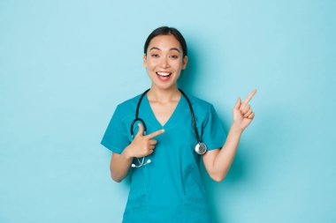 Covid-19, sosyal uzaklık ve koronavirüs salgını konsepti. Mutlu, güler yüzlü Asyalı hemşire, doktor ya da stajyer doktor önlükleriyle sağ üst köşeyi işaret ediyor.