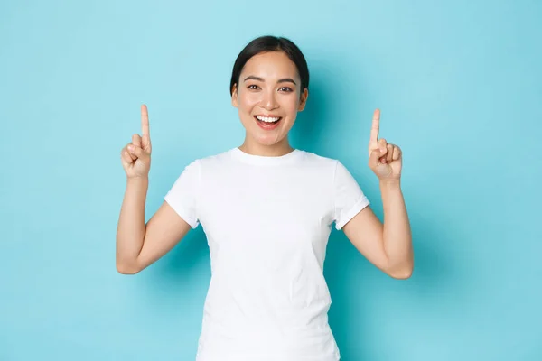 Retrato de menina asiática bonita feliz mostrando promo, demonstrar banner, apontando os dedos para o espaço vazio para o seu anúncio. Coreano feminino alegremente sorrindo para a câmera sobre o fundo azul — Fotografia de Stock