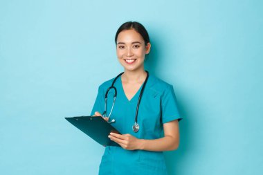 Covid-19, sosyal uzaklık ve koronavirüs salgını konsepti. Gülümseyen Asyalı kadın hemşire, önlüklü doktor stajyeri elinde dosya, hasta kontrolü yaptırıyor, teşhis yazıyor.