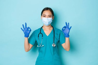 Covid-19, sosyal uzaklık ve koronavirüs salgını konsepti. Tatmin olmuş gülümseyen Asyalı kadın doktor, sağlık maskeli hemşire, önlük, lastik eldiven, her şeyin yolunda olduğundan emin ol.