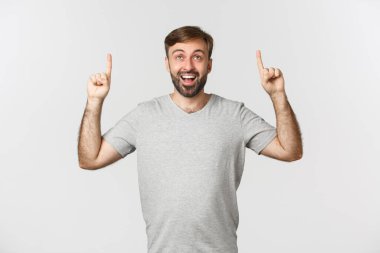 Sakallı mutlu ve şaşırmış bir adamın portresi, büyülenmiş görünüyor ve parmaklarını havaya kaldırıyor, logoyu gösteriyor, beyaz arka planda duruyor.