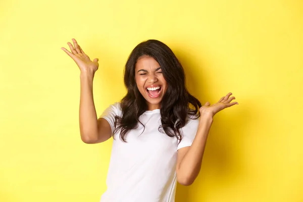 Retrato de menina afro-americana alegre, gritando de alegria e celebrando, alcançar objetivo ou ganhar algo, de pé sobre fundo amarelo — Fotografia de Stock