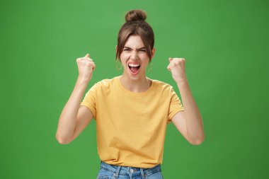 Öfkeli ve güçlü duygusal kadın sarı tişörtlü, dişleri açık, tezahürat yaparak bağıran kendini adamış, favori takımı destekleyen, zaferde yumruklarını sıkarak kazanmak isteyen.