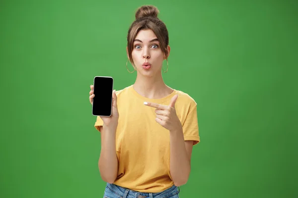 Porträtt av fascinerad kvinna kan inte vänta med att använda nya smartphone hålla telefonen och peka på mobiltelefon skärmen vikbara läppar med spänning och intresse att presentera nya enhet modell i beredskap över grön vägg — Stockfoto
