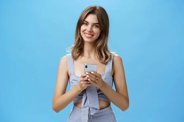 Friendly pleasant good-looking woman in matching outfit holding smartphone over chest tilting head smiling broadly showing cute gapped teeth being delighted after reading heartwarming message — Stock Photo, Image