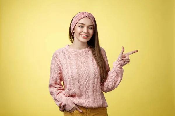 Стиль жизни, люди, указывающая концепция. Привлекательная молодая девушка с длинными прямыми волосами в свитере указывая в сторону с помощью переднего пальца, указывая копия пространства улыбаясь веселый, положительный поверх желтой стены — стоковое фото