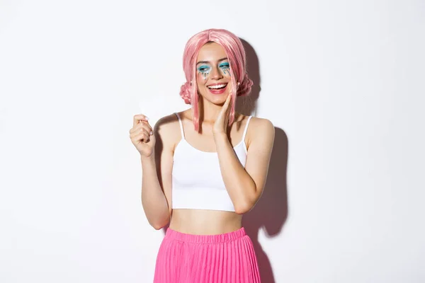 Wizerunek zadowolony stylowa dziewczyna w różowej peruce patrząc szczęśliwy na karcie kredytowej, marzy o zakupach, stojąc nad białym tle — Zdjęcie stockowe