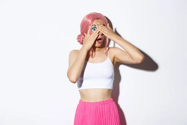 Retrato de una joven bonita tonta con peluca rosa y traje de Halloween, ojos cerrados pero mirando a través de los dedos a algo interesante —  Fotos de Stock