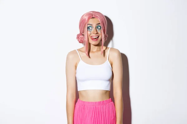 Retrato de menina festa animado mostrando língua e sorrindo, olhando para a esquerda com expressão feliz, vestindo peruca rosa para a celebração do dia das bruxas, de pé sobre fundo branco — Fotografia de Stock