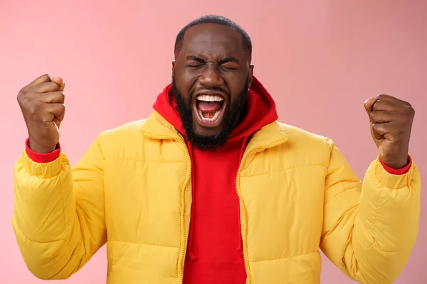 Hombre afroamericano guapo animándose a sí mismo poner esfuerzo apretó los brazos gritando cerca de los ojos levantar las manos aumentar la confianza, de pie fondo rosa expresar rabia liberar emociones — Foto de Stock