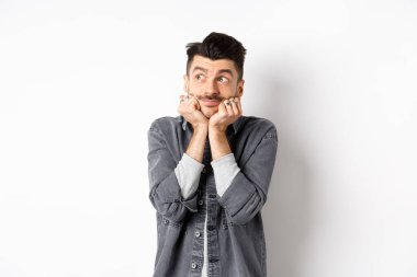 Heyecanlı genç adam sol üst köşede rüya gibi görünüyor, paketi bekliyor, hayal görüyor ya da hayal kuruyor, beyaz arka planda duruyor.