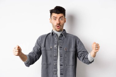 Kafası karışmış bir adam büyük bir nesne tutuyor ve şok olmuş görünüyor, büyük bir şeyi şekillendiriyor, beyaz arka planda duruyor.
