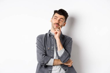 Düşünceli yakışıklı adam dalgın dalgın bakıyor, seçim yapıyor, beyaz arka planda duruyor.