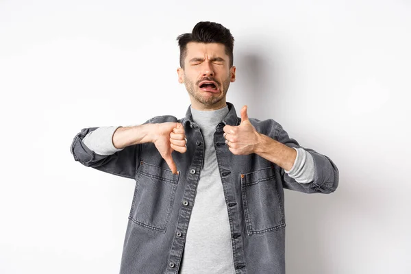 Droevige man huilen en tonen duimen naar beneden, zeuren en klagen, staan teleurgesteld tegen witte achtergrond — Stockfoto