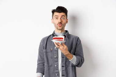 Adam doğum gününü kutluyor, pastaya mum üflüyor ve dilek tutuyor, beyaz arka planda duruyor.