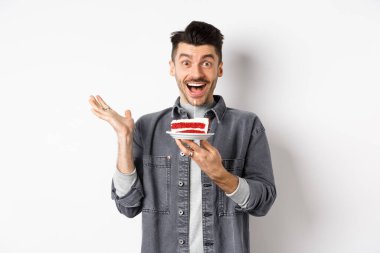 Heyecanlı bir adam doğum gününü kutluyor, mutlu görünüyor, elinde mumla pasta tutuyor, dilek tutuyor, beyaz arka planda mutlu duruyor.