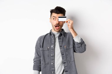 Heyecanlı komik adam logoya bakar ve beyaz arka planda duran plastik kredi kartını gösterir.