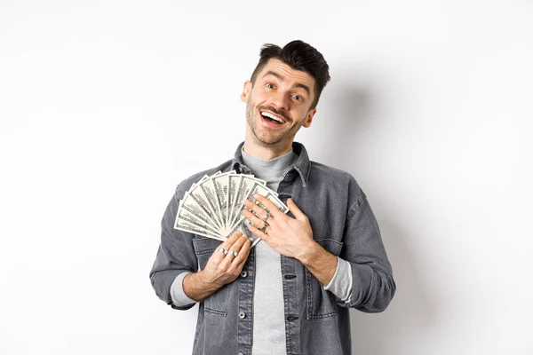Feliz chico sonriente haciendo dinero, abrazando billetes de dólar con la cara aliviada complacido, de pie sobre fondo blanco — Foto de Stock