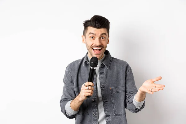 Guapo intérprete sonriente hablando en micrófono, gesticulando y realizando, haciendo discurso con micrófono, de pie sobre fondo blanco —  Fotos de Stock