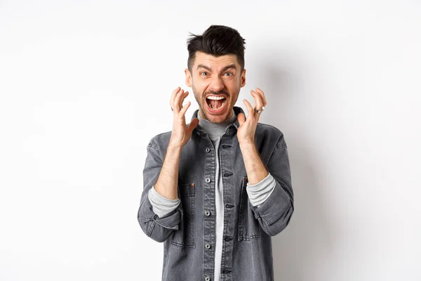 Homem irritado gritando angustiado, perdendo a paciência e gritando frustrado, olhando para algo ruim, de pé sobre fundo branco — Fotografia de Stock