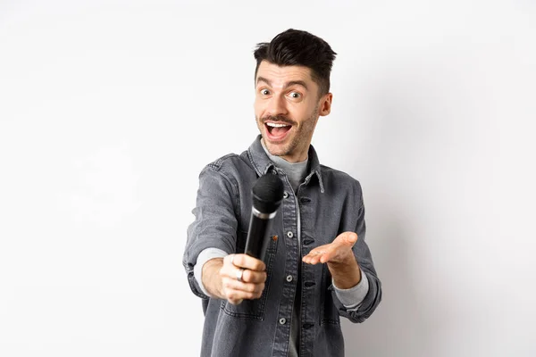 Bel homme souriant étirer la main avec microphone, vous donnant micro, debout sur fond blanc — Photo