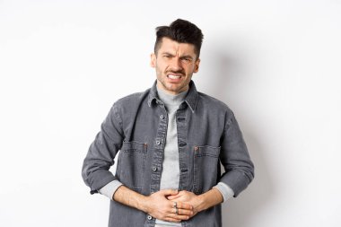 Karnı ağrıyan, karın ağrısı çeken, yemek zehirlenmesi geçiren, ishal olan, beyaz arka planda duran bir adam.