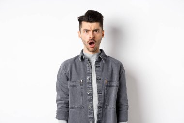 Şok olmuş ve gücenmiş bir adam, kameraya açık ağızla bakıyor, acımasız sözlerle incinmiş, beyaz arka planda hayal kırıklığına uğramış.