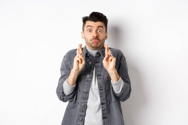 Umut dolu komik adam şans için nefes alıp dua ediyor, dilek tutuyor, haber bekliyor, somurtuyor ve kameraya bakıyor, beyaz arka planda duruyor.