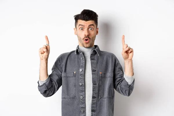 Emocionado hombre mirando la oferta promocional, jadeando sorprendido y señalando los dedos hacia arriba, haciendo un anuncio fresco, de pie sobre fondo blanco — Foto de Stock