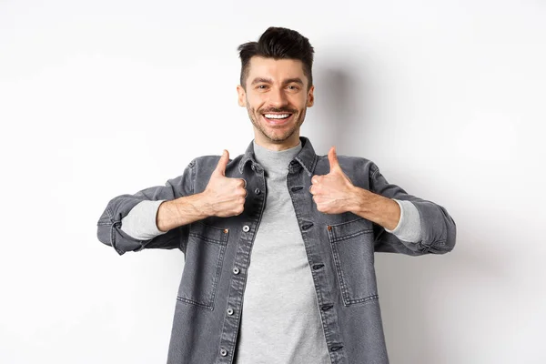 Hombre sonriente guapo mostrando pulgares hacia arriba en la aprobación, alabanza buen trabajo, satisfecho con la buena elección, recomendando algo fresco, de pie sobre fondo blanco —  Fotos de Stock