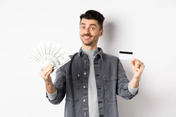 Счастливчик показывает пластиковые кредитки и долларовые купюры, дает выбор, стоя на белом фоне — стоковое фото