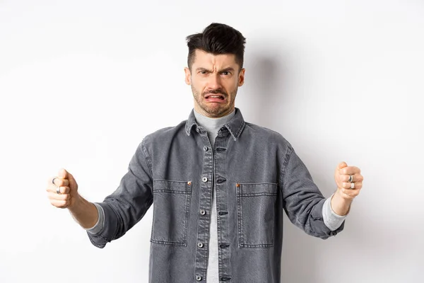 Äcklig kille visar stor storlek objekt och grimacing från motvilja och motvilja, talar om äcklig stor sak, står på vit bakgrund — Stockfoto