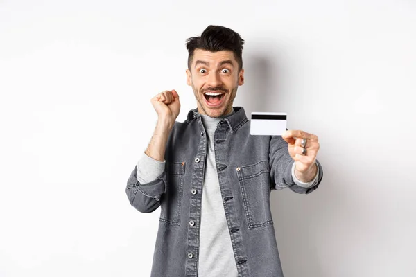 Homem feliz grito de emoção e mostrar cartão de crédito de plástico, recomendando banco, de pé sobre fundo branco — Fotografia de Stock