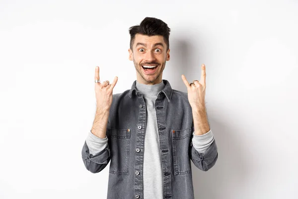 Gelukkig en opgewonden man tonen rock op gebaar en plezier hebben, genieten van evenement en glimlachen vrolijk, staan op witte achtergrond — Stockfoto