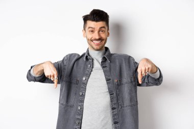 Bıyıklı, mutlu, beyaz bir adam. Gülümsüyor ve özel bir anlaşma yapıyor. Buraya bakmaya davet ediyor, beyaz arka planda duruyor.