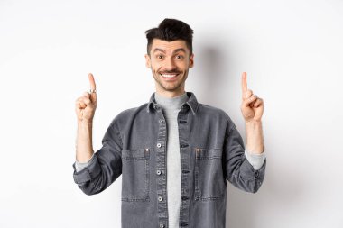 Heyecanlı genç adam gülümsüyor ve reklamını yapıyor, reklam teklifini işaret ediyor, beyaz arka planda duruyor.